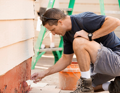 Person painting the exterior of a building with a paintbrush.
