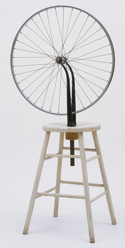 A bicycle wheel mounted upside down on a wooden stool.