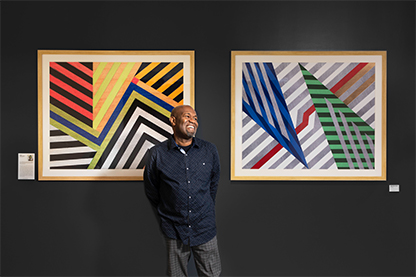 Artist Rudolph Jean-Louis stands in front of two of his prints