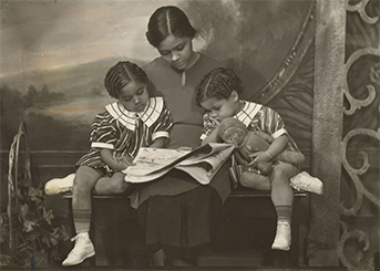 A woman reading a newspaper to two children