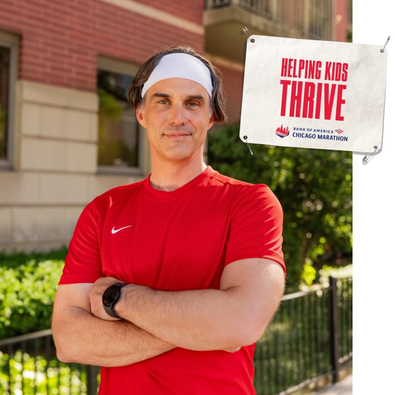 Tim standing outdoors with an image of a bib that reads “HELPING KIDS THRIVE”