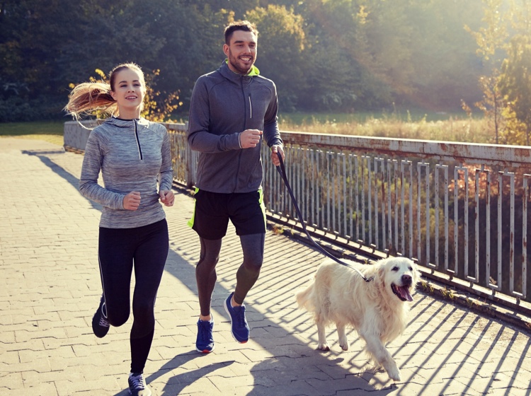 Man and woman running outside with dog