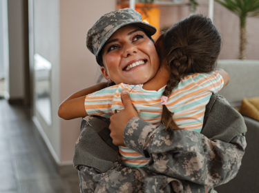Person in military uniform hugging a young child