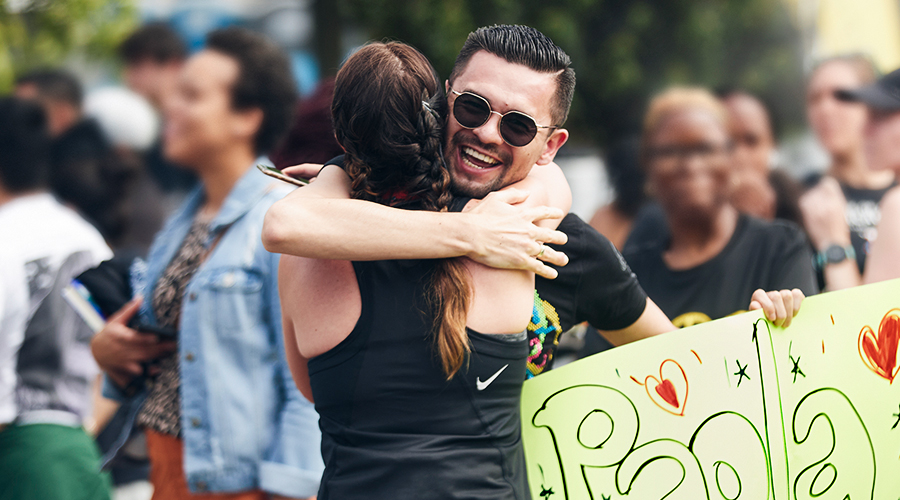 A spectator smiling as he holds a sign and hugs a runner​ 