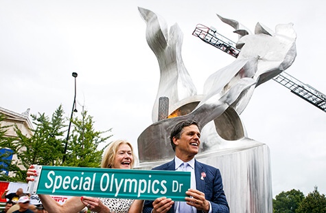Two people pose with sign in front of monument
