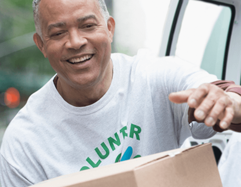 A man carrying a cardboard box smiles as he volunteers