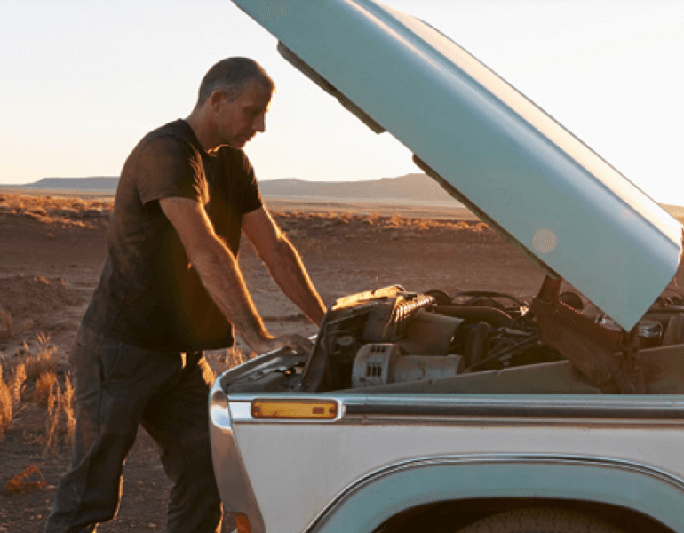 A man reviews his car engine while standing on the side of the road