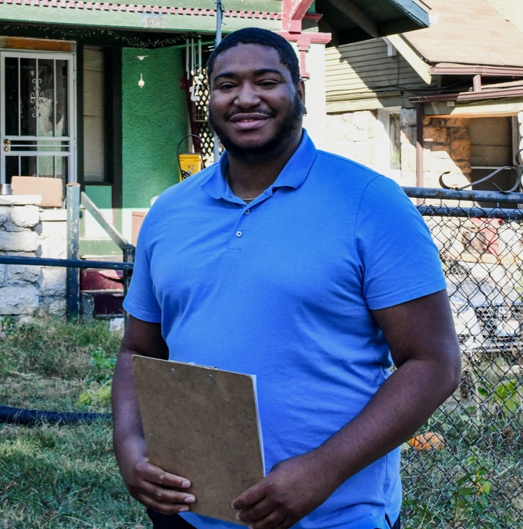 Man holding a clipboard smiling in front of a house