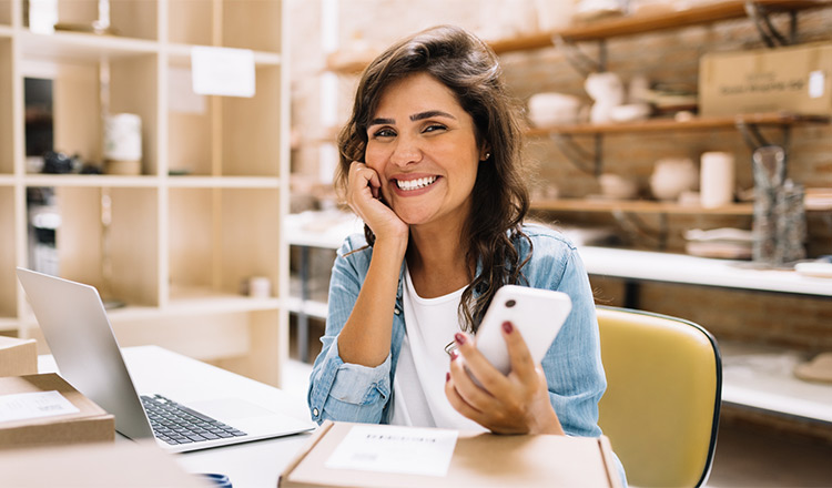 Woman smiling with phone in hand in front of computer.