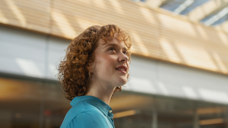 Person with curly hair in a blue shirt looking upward in a brightly lit indoor space.