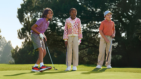 Three kids on a golf course putting green, excited about making an excellent shot