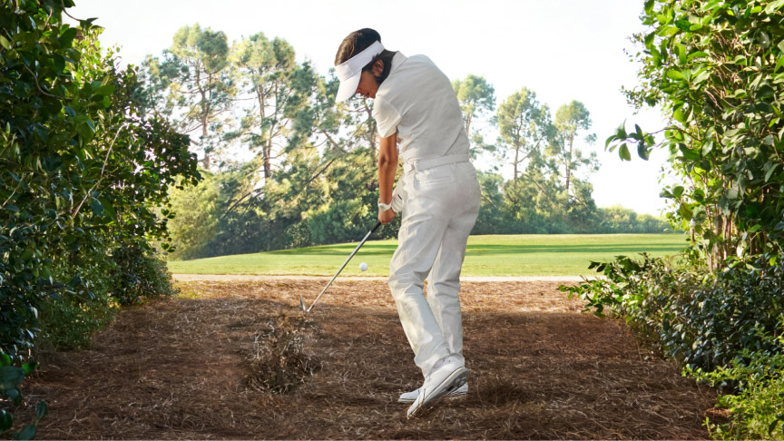 A young golfer chips their ball from a rough section toward the fairway