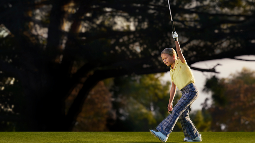 A young golfer holding her club high after a long drive