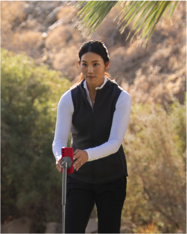 A woman, Jeehae Lee, using AI technology on a smartphone to record and analyze a golfer’s swing.