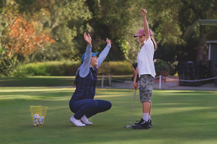 A parent high-fiving her daughter on a golf course 