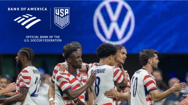 Photograph of a group of male soccer players celebrating on a field.