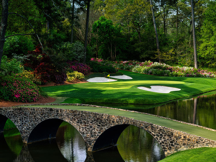 A manicured green with a yellow flag marking the hold sits between two white sand bunkers as sunlight casts soft shadows across the course.