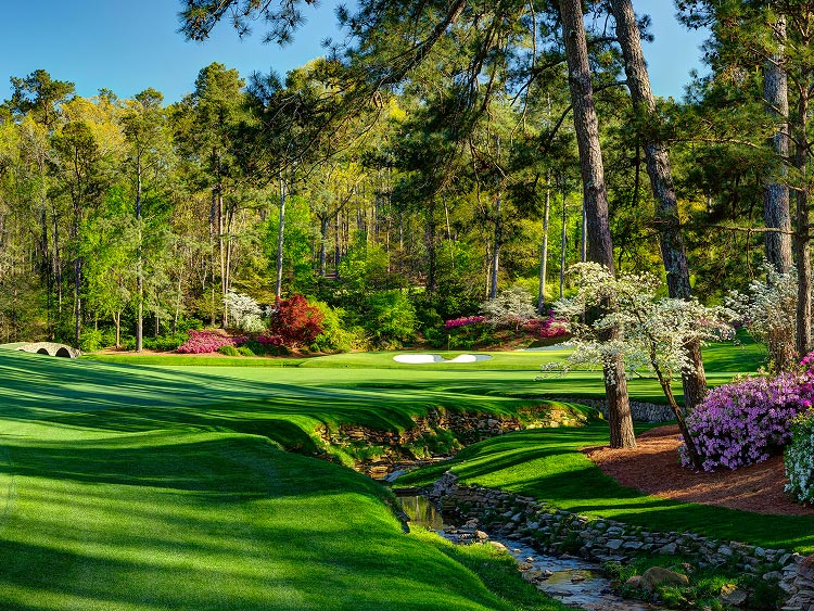 In the distance, a putting green sits beside a white sand bunker with shadows casting long shadows across the grass.