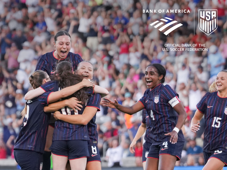 Photograph of a group of female soccer players celebrating on a field.