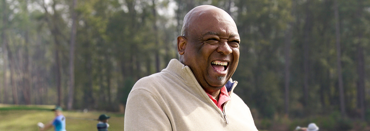Ira Miller smiles on the golf course as players swing in the background