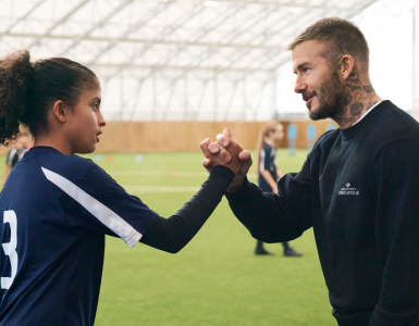 Sir David Beckham shaking hands with a young soccer player.