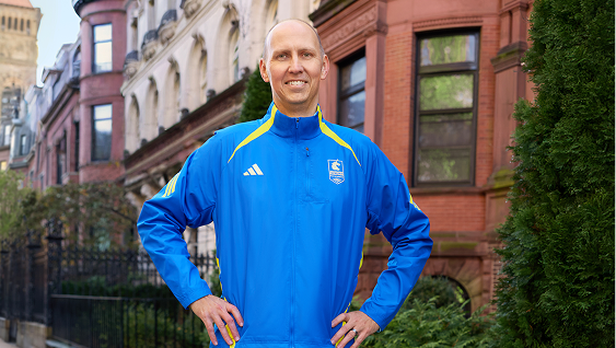 A runner stands proud on a Boston Street in front of brownstone buildings and lush, green bushes