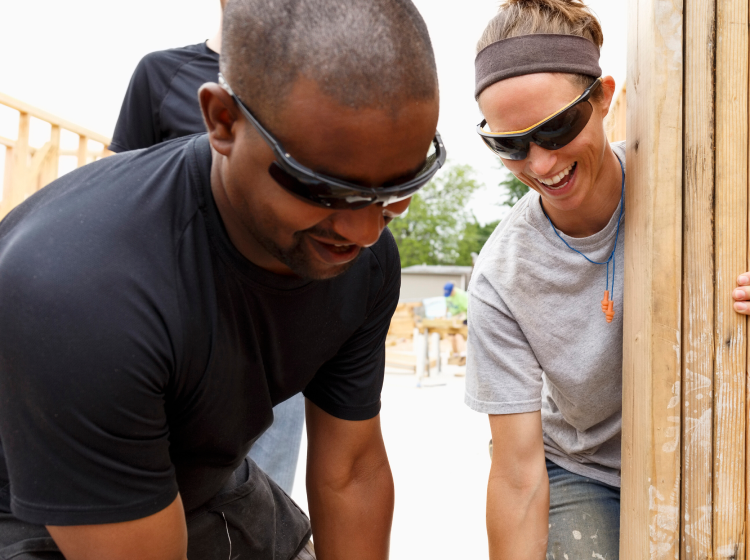 Three young volunteers smiling as they work on home framing