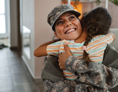 Person in military uniform hugging a young child