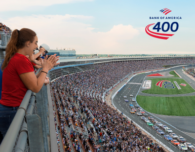 Fans watching a race at a crowded speedway from the grandstands.