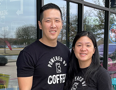 The couple Tommy and Lisa Lau standing out of their Cypress, Texas coffee shop, wearing t-shirts that say “powered by coffee”