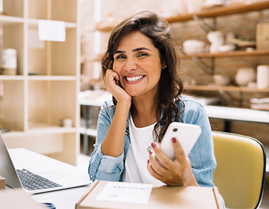 Woman smiling with phone in hand in front of computer.