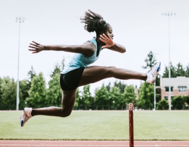 African American girl running over hurdle