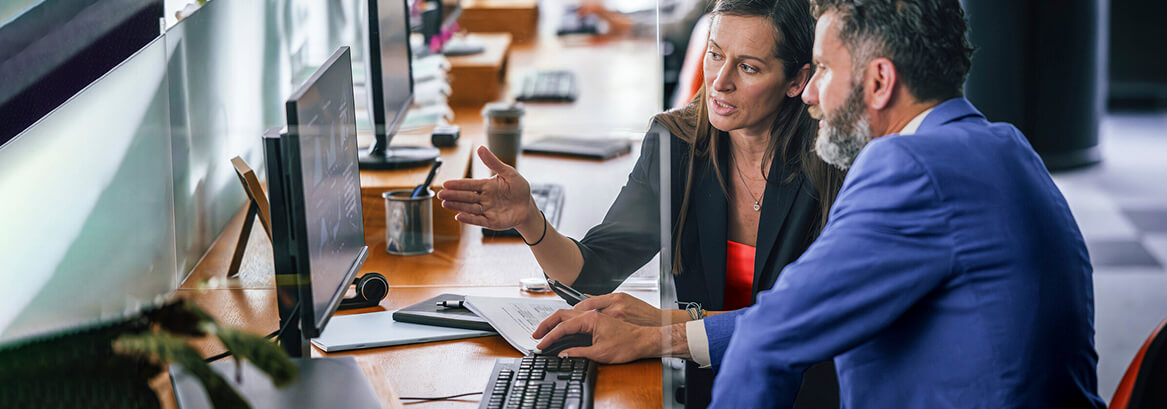 Two colleagues reviewing information on a computer screen in an office workspace
